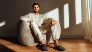 Man sitting relaxed in a light-coloured armchair by the window, wearing grey Giesswein wool slippers
