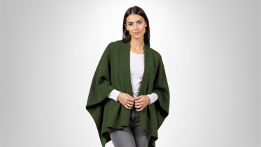 Woman wearing dark green merino poncho over white T-shirt and grey jeans against light grey background