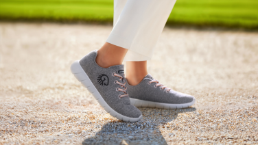 Side view of person wearing white trousers and grey Giesswein Merino sneakers on a gravel path outdoors