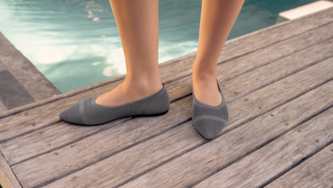  A close-up of two feet in grey knitted ballet flats on a wooden walkway by the pool.