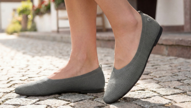 A close-up of feet in grey Giesswein knitted ballerina flats, standing on cobblestones.
