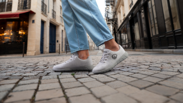 Close-up of feet in grey Giesswein Merino Runners on cobblestones in an urban street scene